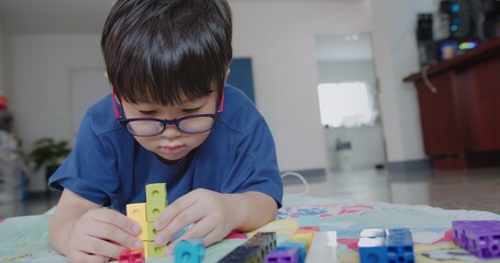 Portrait attractive smart cute Asian child boy wearing eyeglasses enjoy playing colorful tower...