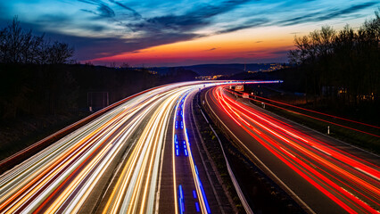 Colorful panorama of German motorway A45 called “Sauerlandlinie“ with curved lanes at blue hour twilight after sunset near Hagen. Colorful light traces of passing cars and blue flash lights. - obrazy, fototapety, plakaty
