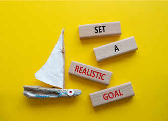 Set a realistic goal symbol. Concept words Set a realistic goal on wooden blocks. Beautiful yellow background with boat. Business and Set a realistic goal concept. Copy space.