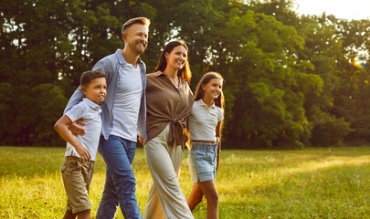 Happy family strolling in nature. Cheerful, smiling father, mother and children in casual clothes...