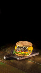 Hamburguer com carne, queijo derretido, alface, tomate e cheddar sobre fundo de madeira