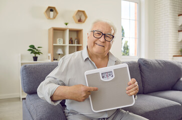 Healthy retirement. Cheerful retired man shows electronic floor scale that he holds in his hands....