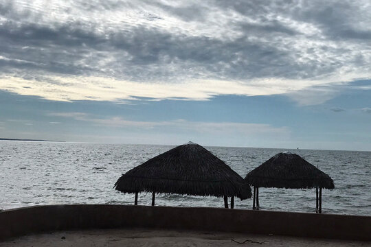 Two grass huts on a beach in Mahajanga, Madagascar at sunset dusk time. Cool blue skies fading in the background as calm waves wash over the sand.