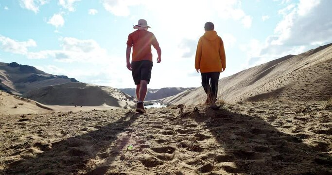 Back view at couple of two hikers walking way along sandy desert area at scenic landscape. Travel recreation in wilderness together and trip tourist trail