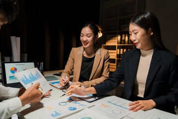 Burning the Midnight Oil: A team of Asian business professionals huddle over illuminated charts and graphs in a dimly lit office, strategizing late into the night. 