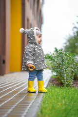 A cute stylish two-year-old toddler girl kid in a gray coat and yellow boots walks outdoors in the city in autumn season 