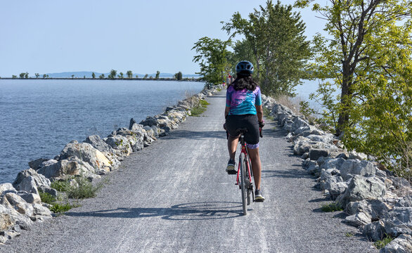 woman riding a bicycle on the colchester causeway in vermont (burlington gravel bike cycling path across lake champlain to south hero island line rail trail) cyclocross tires, from behind (no face)