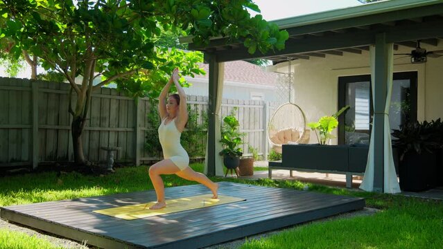 Woman standing in yoga pose on mat while practicing in beautiful tropical backyard garden