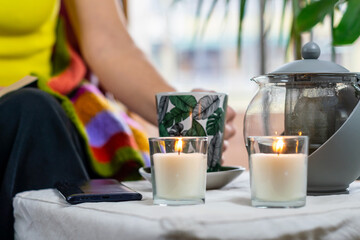 Relaxed Scene: Mug Held by a Woman's Hand, Smartphone, Scented Candles and Houseplants Create a...