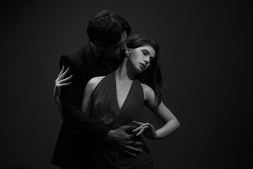 A passionate portrait of a man in a black suit and a woman in a red dress on a dark background,...