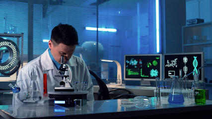 Male scientist sitting in a research lab with test tubes and flasks. A doctor in a white coat is...