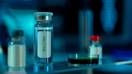 Close up of glass vial with vaccine and petri dish on table in research lab or hospital. Vials with...