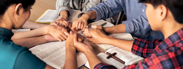 Cropped image of diversity people hand praying together at wooden church on bible book while hold...