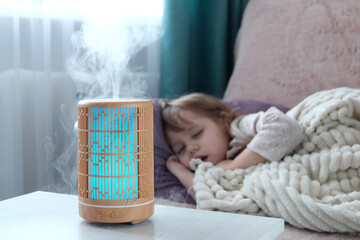Wooden diffuser, blue light, electric aromatic. A little blonde girl is resting on the sofa. The...