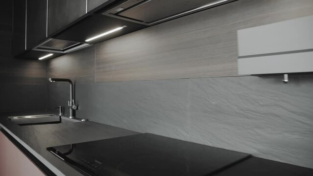 Kitchen sink and faucet, minimalist kitchen interior in black color. Simple well designed modern kitchen interior. Brown ceramic tiles on the wall, kitchen with lighting, slow motion.