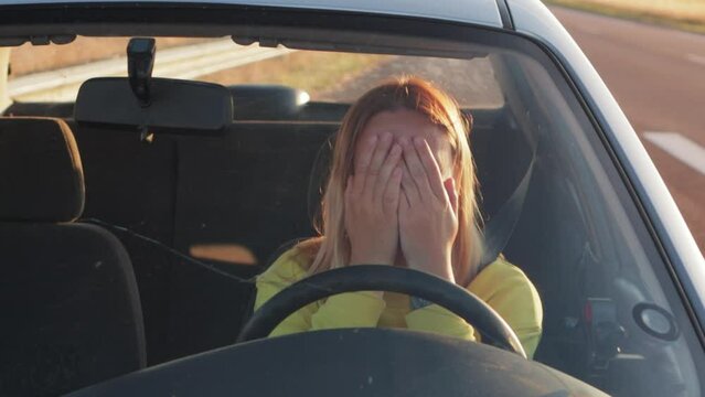 girl in yellow jacket sits behind the wheel of a car sad, holds on to the steering wheel and scream