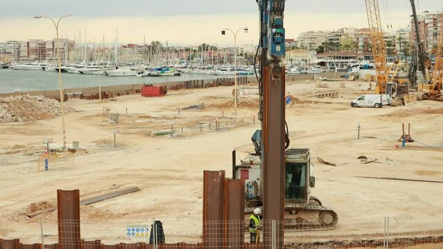 Construction site of public buildings on hills near sea coastline. Cranes during lifting operations
