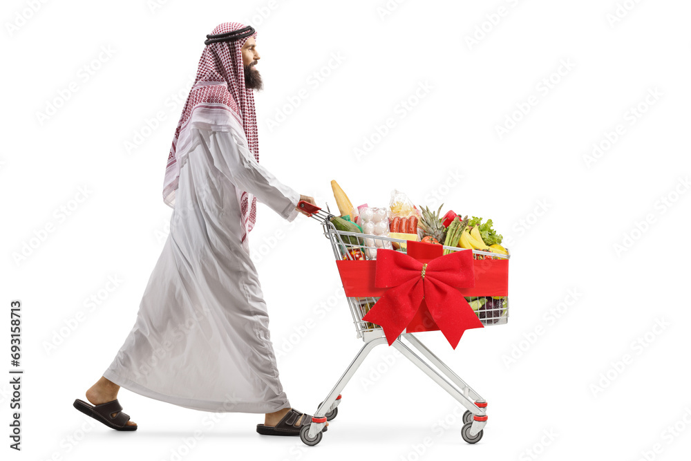 Poster full length profile shot of an arab man walking and pushing a shopping cart with red ribbon