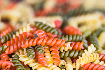 Closeup of colored spiral twisted fusilli pasta on pile with blurred background. Side view a heap...