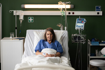 Senior woman in the hospital ward gazes out of the window, deep in thought.