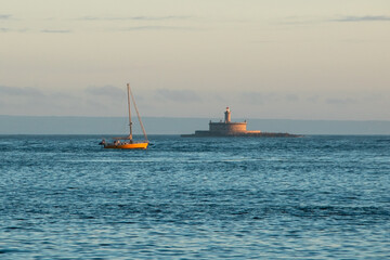 Sailing boat in the sea at sunset with lighthouse in the background