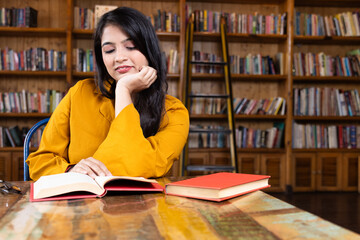 A beautiful young girl business woman or student working or studying in school or collage library or in corporate office sitting with books