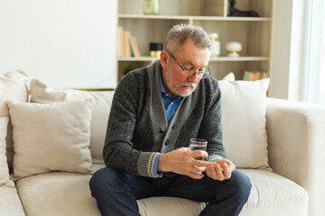 Middle aged senior man holding medical pill and glass of water. Mature old senior grandfather...