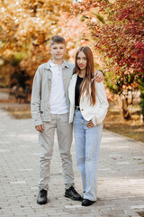 Fototapeta premium Vertical photo of two teenage friends dressed in casual clothes standing next to each other against a background of nature. Best school friends are ready to overcome anything to achieve the goal.