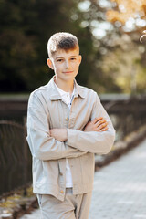 Vertical close-up portrait of a teenager in casual clothes. Happy smiling teenager in autumn park in sunlight. A beautiful child looks at the camera in nature.