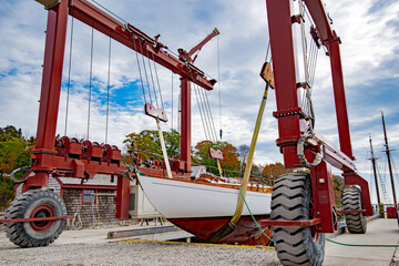 Boat Lift:  A large mobile boat hoist lifts a sailboat on wide straps in preparation for winter at...