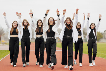 A group of many happy teenage girls dressed in the same outfit having fun and posing in a stadium...