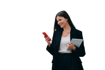 Cheerful brunette in a black suit is standing against transparent background, reading good message, holding a tablet, phone enjoying success at work. A financial consultant reads a review of work