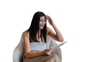 Laughing asian girl with long loose hair sitting in chair with laptop against transparent background tablet loud smiling during video call. Beautiful Korean model relaxing home on weekend.