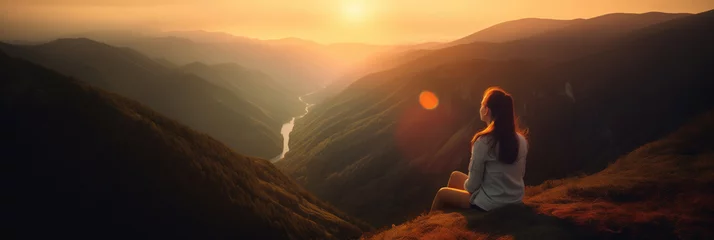 Fotobehang Young woman sitting on a ledge of a mountain and enjoying the beautiful sunset over a wide valley.  © Александр Марченко