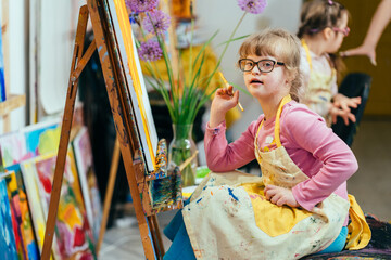 Cute kid artist with down syndrome enjoys creative painting craft at class. Caucasian girl preschooler smile happily, drawing art in classroom. Occupational therapy learning children with disabilities