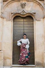 Gorgeous young ethnic woman in traditional dress standing near building door