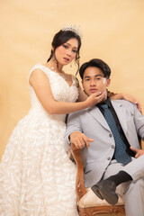 elegant male and female couple poses standing relaxed smiling slightly looking forward girl's hands hold cheeks on arm of chair affectionately indoor photo shot. couple wedding national bride studio