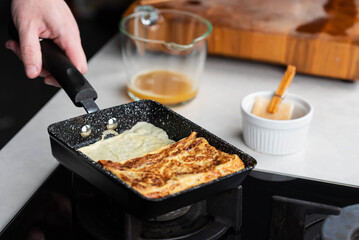 Chef man hands cooking Tamagoyaki or Tamago traditional Japanese Rolled Omelette recipe, made by rolling several layers of cooked scrambled whisking eggs in pan into a rectangular omelet.