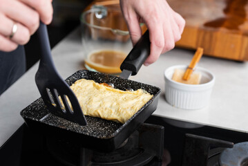 Chef man hands cooking Tamagoyaki or Tamago traditional Japanese Rolled Omelette recipe, made by rolling several layers of cooked scrambled whisking eggs in pan into a rectangular omelet.