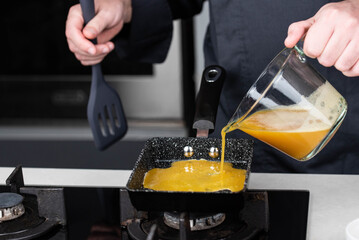 Chef man hands cooking Tamagoyaki or Tamago traditional Japanese Rolled Omelette recipe, made by rolling several layers of cooked scrambled egg in pan into a rectangular omelet.