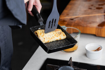 Chef man hands cooking Tamagoyaki or Tamago traditional Japanese Rolled Omelette recipe, made by rolling several layers of cooked scrambled egg in pan into a rectangular omelet.