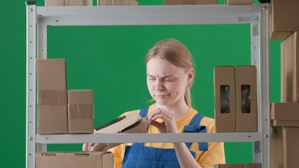 Framed on a green background, chromakey. Depicts a young woman in uniform. Demonstrates a worker, a storekeeper in a warehouse. She holds an open box in her hands and examines it skeptically