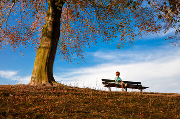 A boy on a bench in an autumn park