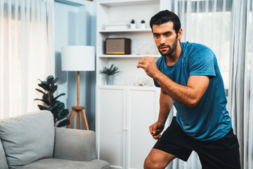 Athletic and sporty man running posture at home body workout exercise session for fit physique and healthy sport lifestyle at home. Gaiety home exercise workout training. - obrazy, fototapety, plakaty