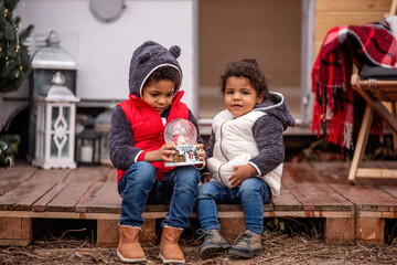 African American boy and girl are sitting at the camper on wooden pallets, playing with a Christmas...