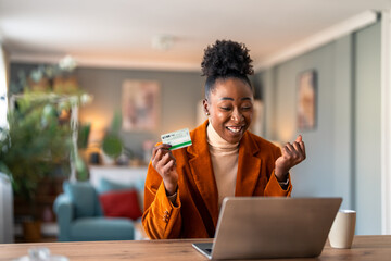 Enthusiastic business woman feeling excited looking at laptop screen holding credit card, holding fist in yes gesture satisfied with online payment possibilities rejoicing approved loan in home office