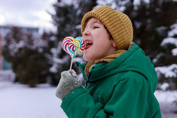 Smiling boy licking a lollipop in winter surrounding