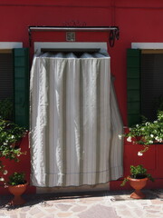 Porte et rideaux blancs, mur rouge, et volets verts, à Burano (Venise, Italie)
