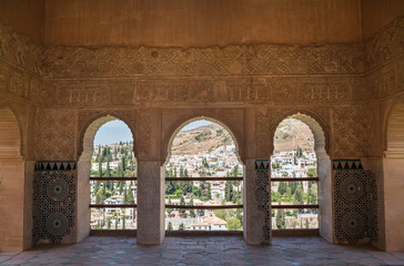 Beautyfull stucco walls decoration with arches in Mexuar section in Nasrid palace with Albacin old town view, Alhambra castle, Andalusia, Spain. The art of Moorish architecture and traveling concept.