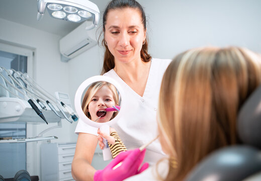 Little girl looking at mirror while dentist doctor doing teeth prevention with excavator and mirror medical tools in stomatology clinic. Healthcare, kid's health and medicare industry concept image.